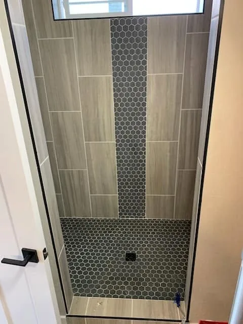 Wood-look tile shower with a dark hexagon tile accent stripe and matching hex floor
