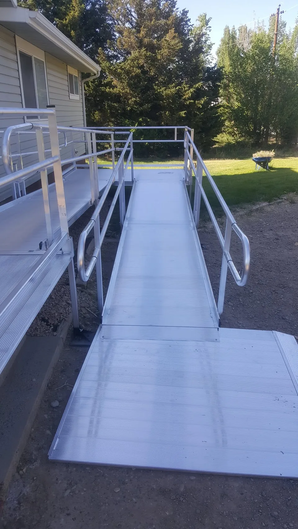 Aluminum wheelchair ramp with handrails along the side of a house