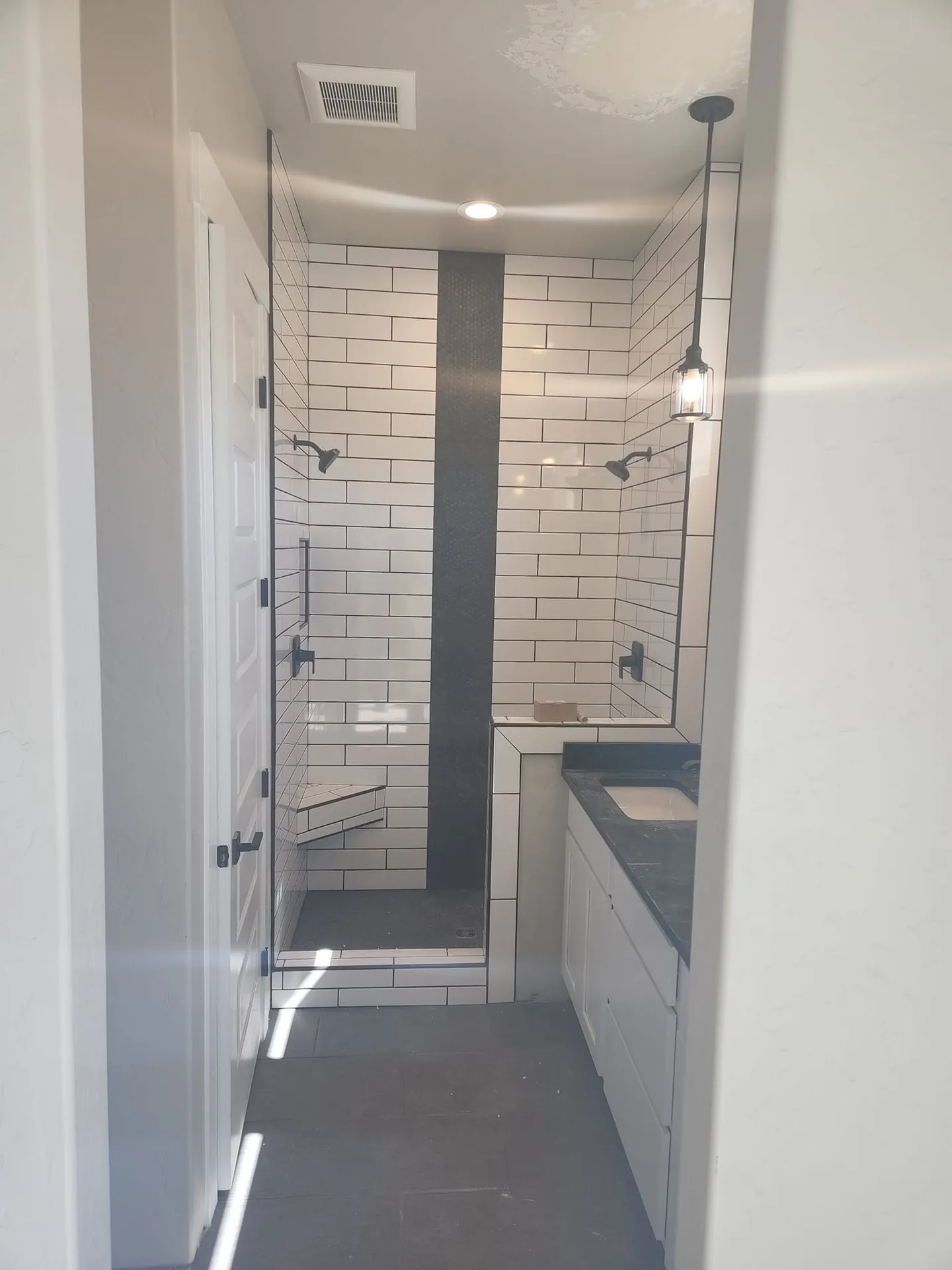 Walk-in shower with white subway tile, a dark tile accent stripe and a built-in bench